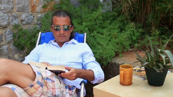 Человек, читающий книгу в саду — стоковое видео