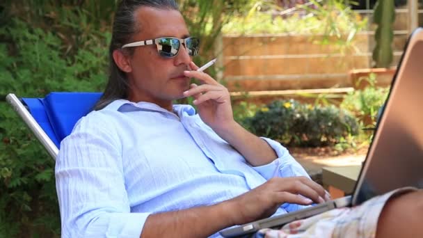 Mann benutzt Laptop und raucht Zigarette — Stockvideo