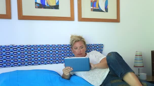 Жінка лежить на ліжку і використовує цифровий планшет — стокове відео