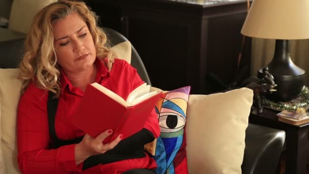 Painful woman sitting on a sofa and reading book — Stock Video