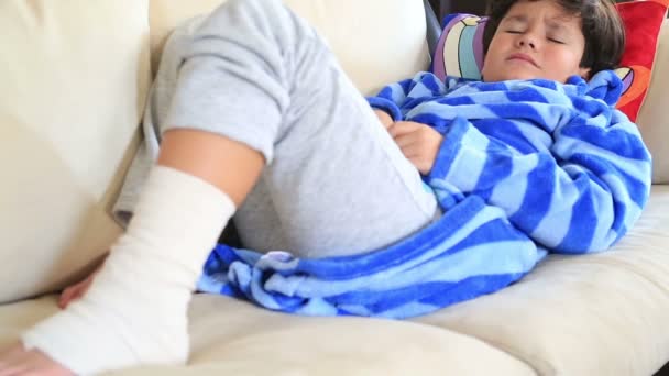 Ребенок с повязкой на ноге, лежащий на диване — стоковое видео
