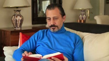 Adam kanepede oturup kitap okuyor.