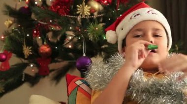 Noel ağacın önünde oturup Noel Baba şapkası ile mutlu çocuk