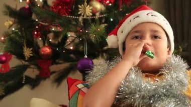 Noel ağacın önünde oturup Noel Baba şapkası ile mutlu çocuk