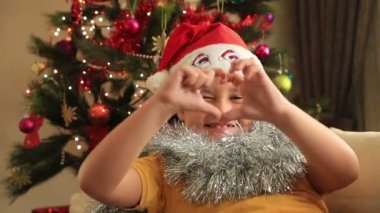 Noel ağacın önünde oturup Noel Baba şapkası ile mutlu çocuk