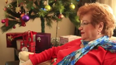 Gülümseyen kırmızı giysili Noel ağacının yanında oturan Olgun kadın