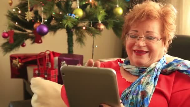 Ώριμη γυναίκα χρησιμοποιώντας την ψηφιακή δισκίο κοντά το χριστουγεννιάτικο δέντρο — Αρχείο Βίντεο