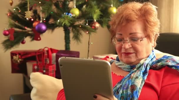 Ώριμη γυναίκα χρησιμοποιώντας την ψηφιακή δισκίο κοντά το χριστουγεννιάτικο δέντρο — Αρχείο Βίντεο