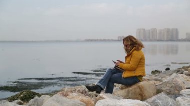 Deniz tarafında oturan ve akıllı telefon kullanan kadın