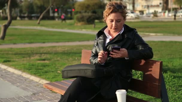 Femme d'affaires utilisant un téléphone intelligent pendant la pause déjeuner dans le parc de la ville — Video