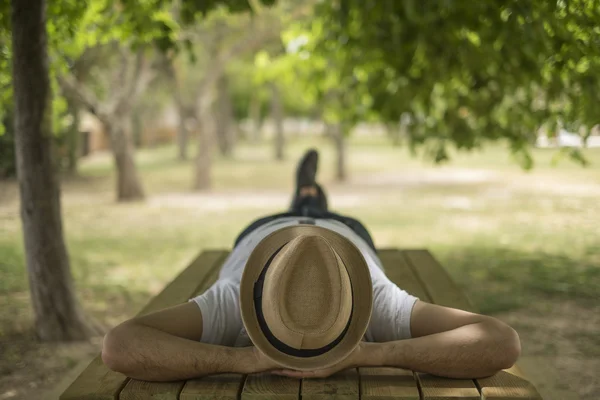 Jeune homme reposant portant un chapeau de paille couché sur une table en bois Images De Stock Libres De Droits