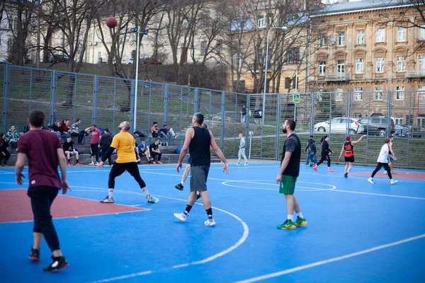 Parktaki spor sahasında basketbol oynayan bir grup erkek.