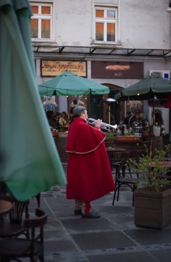 Antik Lviv şehrinin avlusunda, kırmızı ceketli bir trompetçi müşterileri bir kafeye çağırır.
