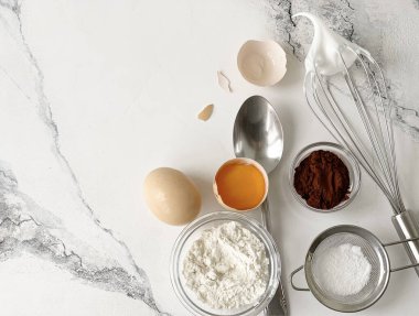 Mutfak gereçleri, çırpma, yumurta, un, beyaz bir masada kakao.