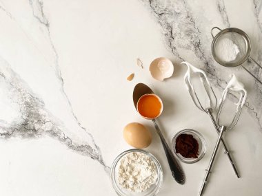 Mutfak gereçleri, çırpma, yumurta, un, beyaz bir masada kakao.