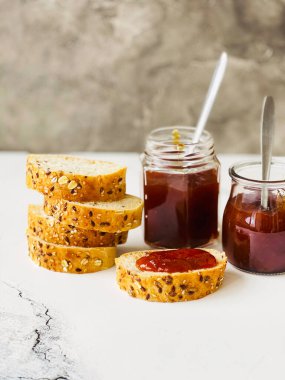 Kavanozlarda kayısı reçeli ve beyaz bir masada kahvaltı için ekmek.
