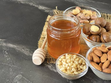 Fındık karışımı: badem, kaju, çam fıstığı, macadamia ve bal siyah bir masada.