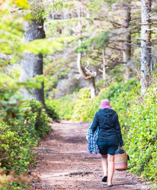 Yağmurluk giymiş bir kadının elinde bir kovayla parkta yürüdüğünü gördüm. Vancouver Adası, BC, Kanada-9 Ağustos 2021. Sokak manzarası, seyahat fotoğrafı, seçici odak,
