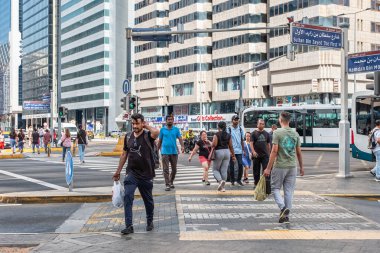 Şehir iş alanında iş çıkış saatinde, Abu Dabi BAE caddelerinden geçen zebra üzerinde yürüyen yayalar. Bir sürü insan caddeyi geçiyor. Zebra caddesindeki kalabalık sokak insanları 19 Nisan 2025 'te kesişiyor