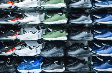 Ayakkabı mağazasının içinde çeşitli erkek ayakkabıları sergileniyor. Duvarda bir sürü spor ayakkabısı sergisi. Modern, yeni şık spor ayakkabıları erkekler ve kadınlar için koşu ayakkabıları. Spor ve günlük ayakkabılar.