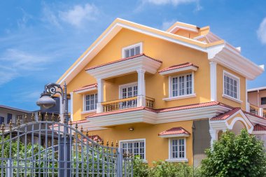 Mavi arka planı olan tipik klasik bir ev. Klasik görünüşlü ve ön bahçeli, iki katlı, özel sarı bir aile evi. Lüks ev dış görünüşü. Kimse.