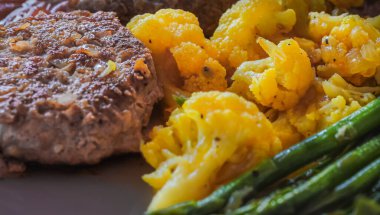 Izgara köfteli bifteği pişmiş sebzelerle kapat. Karnabahar, kuşkonmaz ve pirzola tabakta servis edilir. Sağlıklı konsept yemek, hiç kimse, seçici odaklanma