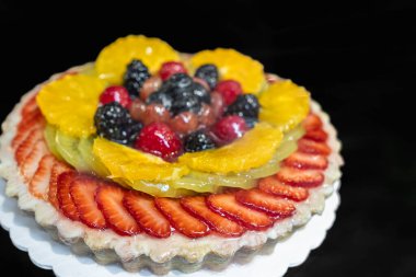 Koyu arkaplanda taze çilek, böğürtlen ve kivi ile süslenmiş pasta. Doğum günü kutlaması, parti ya da festival etkinliği için. Taze yaz meyveleriyle süslenmiş taze pişmiş yuvarlak pasta.