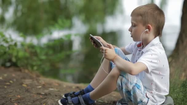 Le garçon lisant le livre dans le parc près de l'eau. (Mise au point sélective )