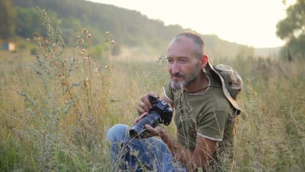 Fotograf wykonuje swoją pracę w słońce wieczór. Mężczyzna zdjęć fotografii w pięknym otoczeniu odkryty. — Wideo stockowe