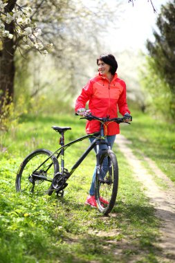 Çiçekli bir bahar bahçesinde bisiklet süren güzel bir kadın. Güzel olgun bir kadın çiçek açan bir bahar bahçesinde kameraya poz veriyor.. 