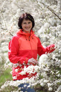 Güzel olgun bir kadın çiçek açan bir bahar bahçesinde kameraya poz veriyor.. 