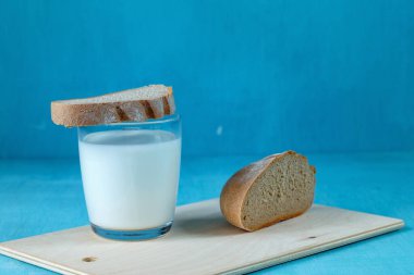 Mavi arka planda bir bardak süt ve siyah ekmek.