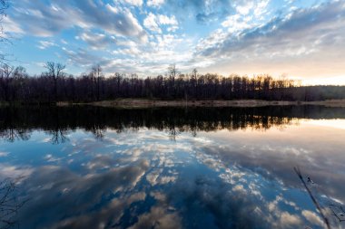 Bulutlar, baharda gün batımında çekilen Pioneer gölünün su yüzeyine yansıyor.