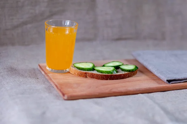 Salatalık dilimli ekmek ve bir bardak portakal suyu bir tahta kesim tahtasının üzerinde tuval arka planında.