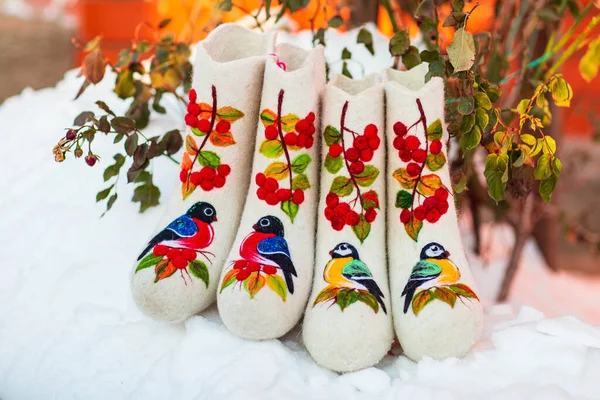 embroidered felt boots taken on a winter evening against the background of snow, bushes and a village house