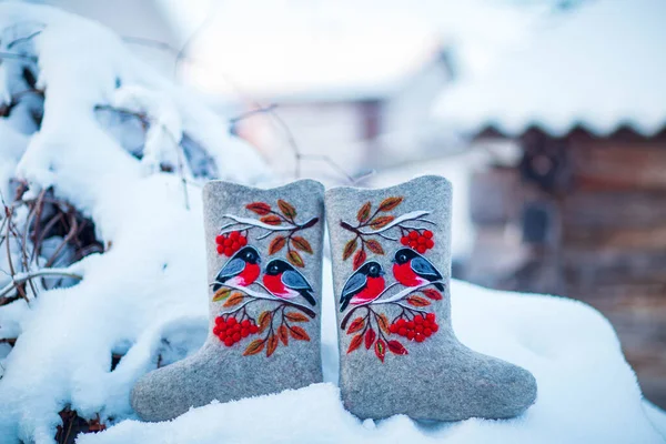 embroidered felt boots taken on a winter evening against the background of snow, bushes and a village house