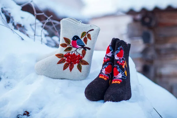 embroidered felt boots taken on a winter evening against the background of snow, bushes and a village house