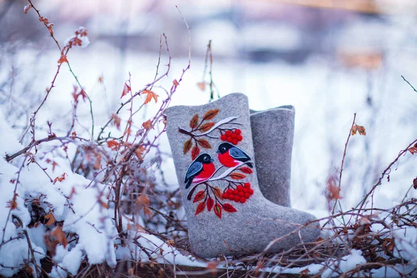 embroidered felt boots taken on a winter evening against the background of snow, bushes and a village house