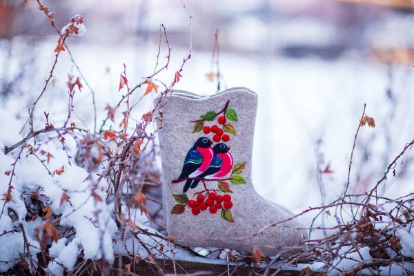 embroidered felt boots taken on a winter evening against the background of snow, bushes and a village house