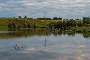 Gökyüzünde bulutların yansımaları ve kıyıda ağaçların olduğu bir gölet, Haziran ayı başlarında Chuvashia 'da çekildi.