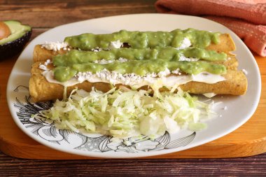 Traditional Mexican food, golden meat tacos (flautas) with guacamole, lettuce, tomato and avocado. clipart