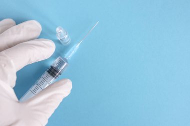 Eldiven giyen bir araştırmacının elinde aşı ve şırıngayla dolu bir şişe. COVID-19 'a karşı korunmak için geliştirilmiş koronavirüs aşısı şişesi. Sağlık ve tıbbi konsept. Mavi arka plan.