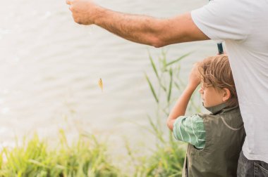 A boy learns how to fish under the guidance of an adult.