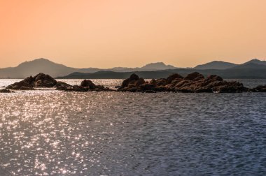 Gün batımında güzel bir deniz. Arkasında kayalar ve dağlar. Sardunya.