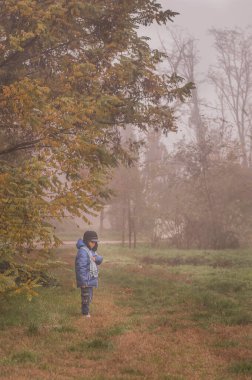 Yalnız çocuk sonbahar sisli ormanında elinde fenerle yürüyor.