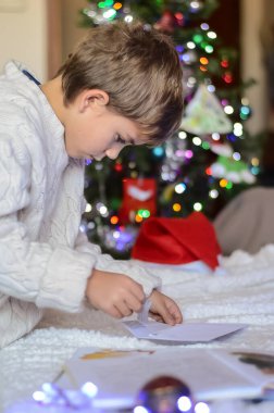 Çocuk Noel Baba 'ya Noel ağacının arka planına karşı bir mektup hazırlıyor..
