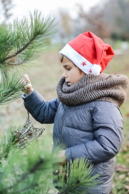 Yeni yıl şapkalı bir çocuk Noel ağacını dışarıda süslüyor.