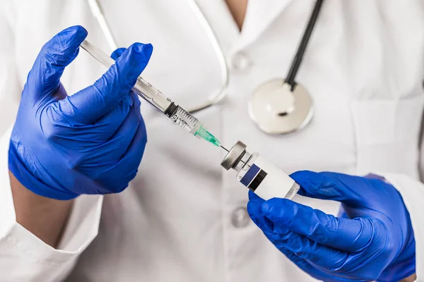 Kadın bir doktor elinde bir şişe ve şırınga ile hastasına aşı vermeye hazırlanıyor.