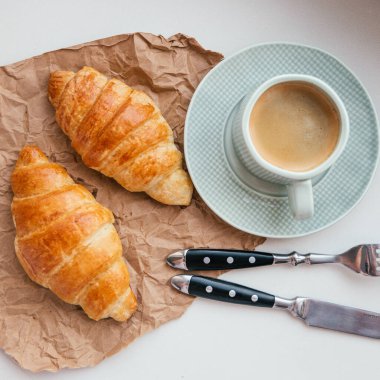 Parşömen üzerine kruvasan, çatal bıçak takımı ve bir fincan kapuçino.
