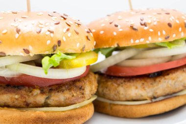 Domatesli, soğanlı, beyaz tabakta salatalıklı büyük bir hamburger manzarası.